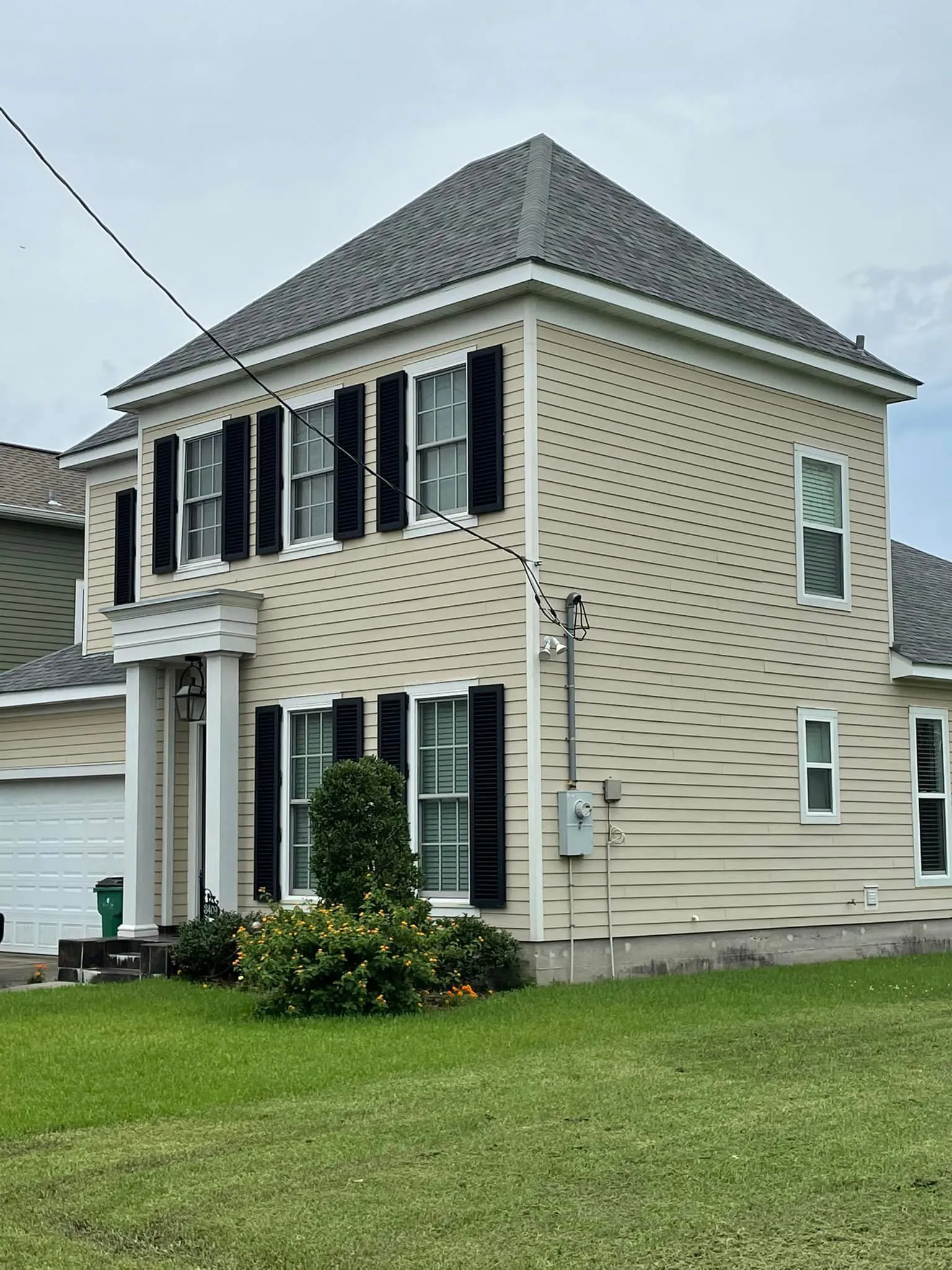 Two-story beige house with black shutters, white trim, and a gabled roof, on a green lawn.