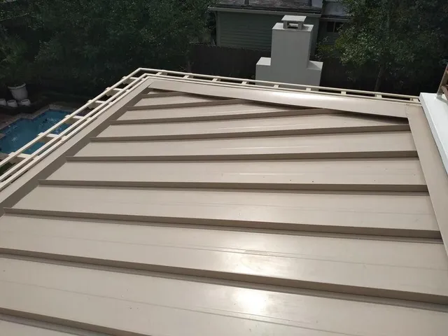 Beige metal roof with horizontal lines, a chimney in the background, and a pool visible to the left.