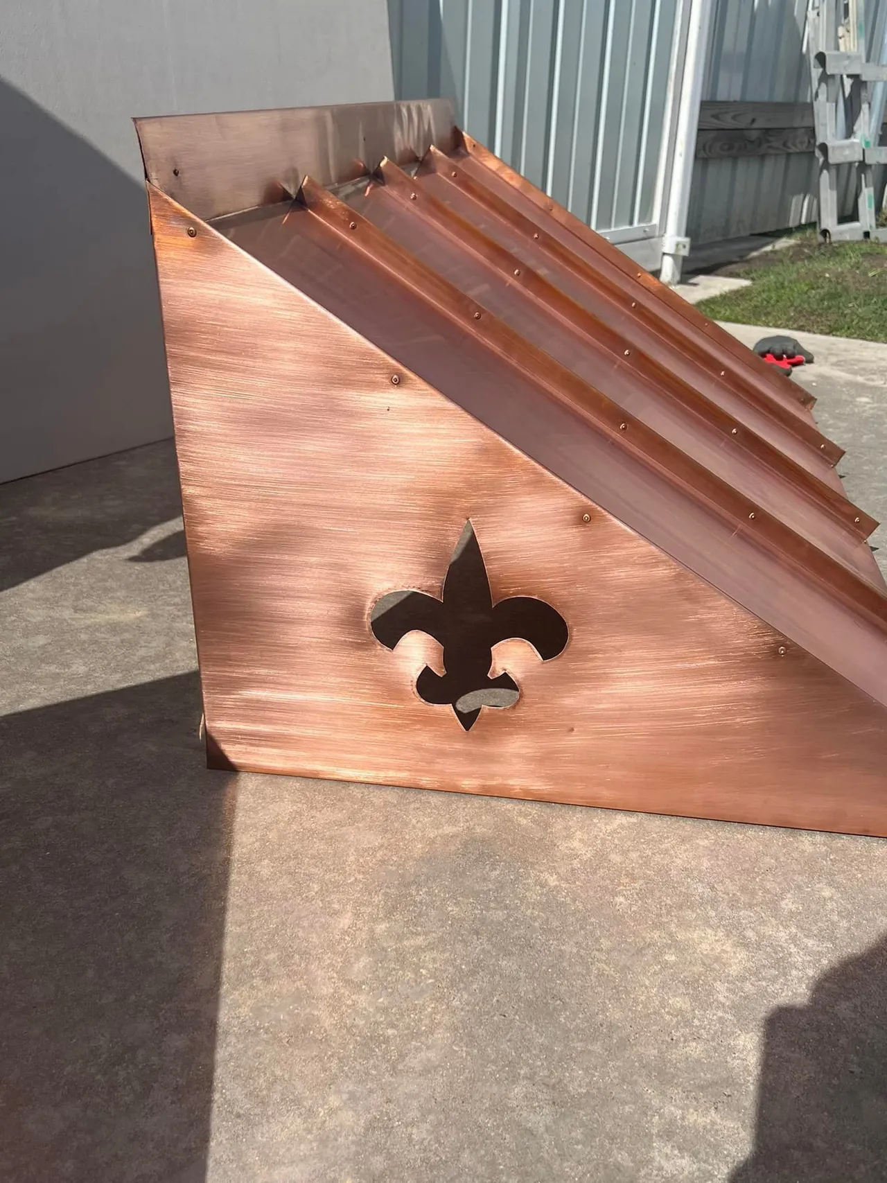 Copper roof flashing with Fleur-de-lis cutout, resting outdoors.