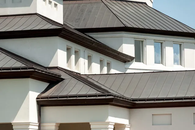 White building with dark brown metal roof and multiple windows.