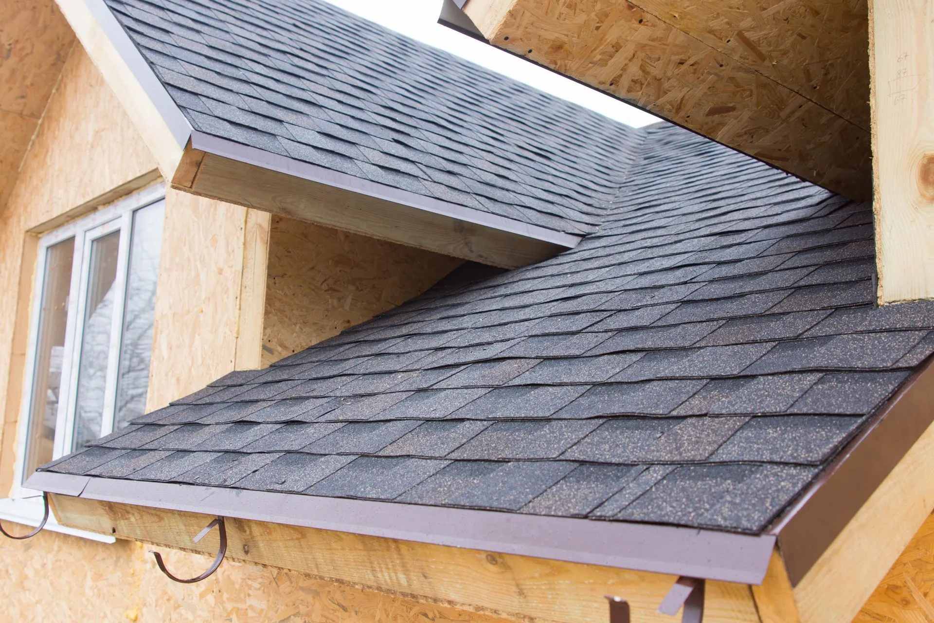 Gray shingle roof on a house with a clear blue sky in the background and power lines.