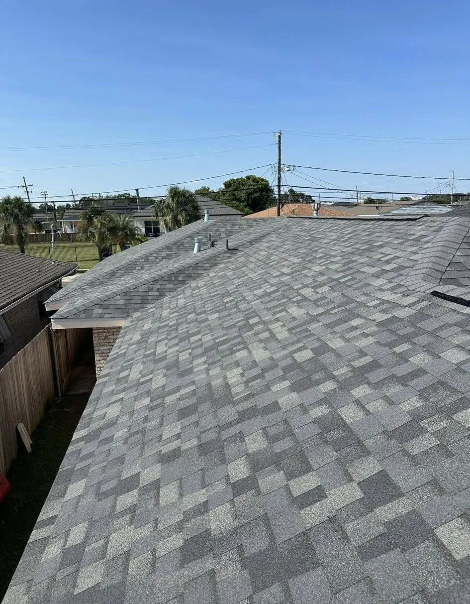 Gray shingle roof on a house with a clear blue sky in the background and power lines.