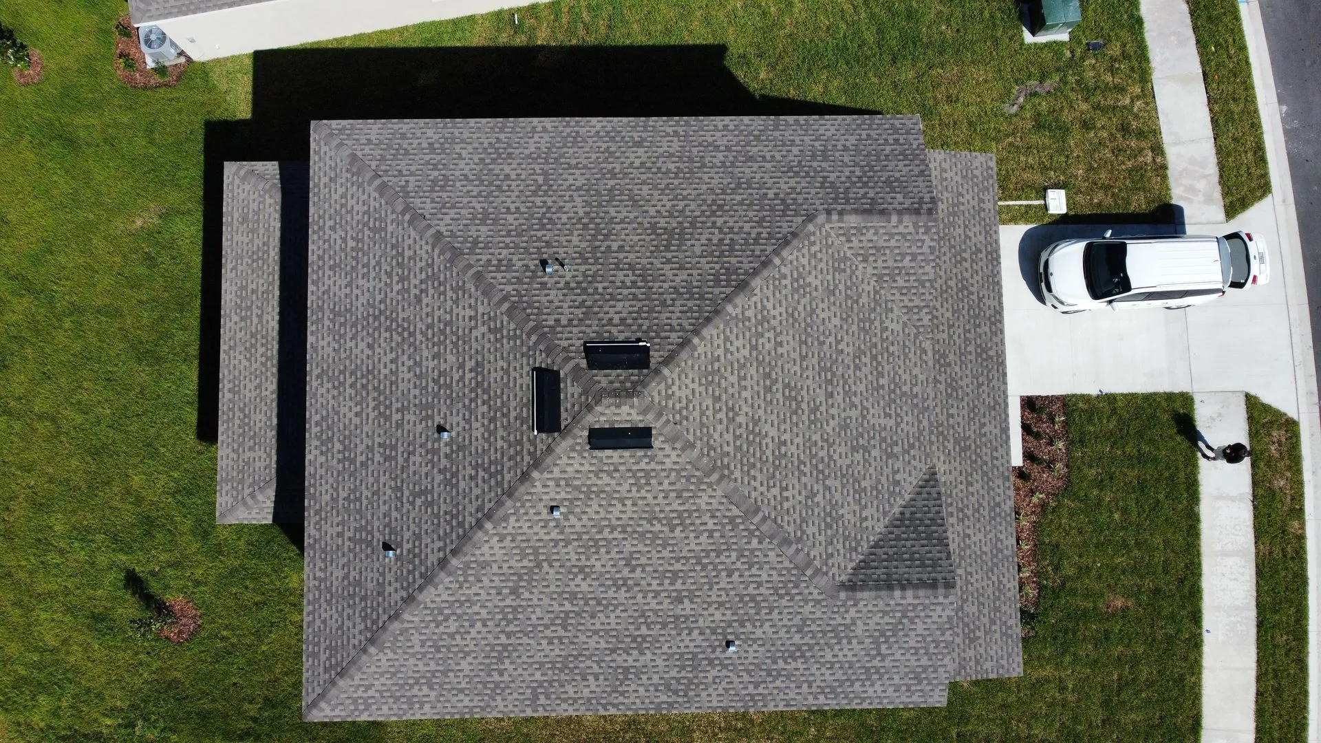 Overhead view of a gray shingled roof with a vehicle parked on a driveway next to a green lawn.