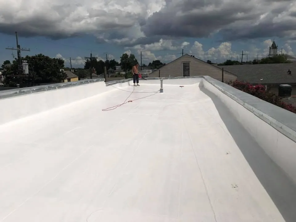 Gray asphalt shingle roof with a vent and a flat section. A house is in the background.